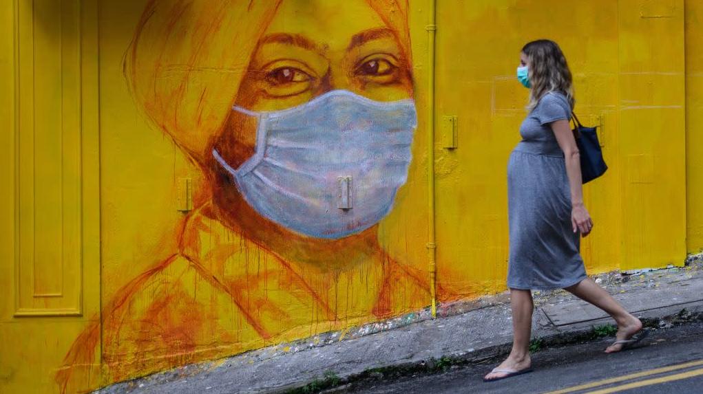 A pregnant woman walks past a street mural in Hong Kong on March 23, 2020. (Photo: Getty Images)