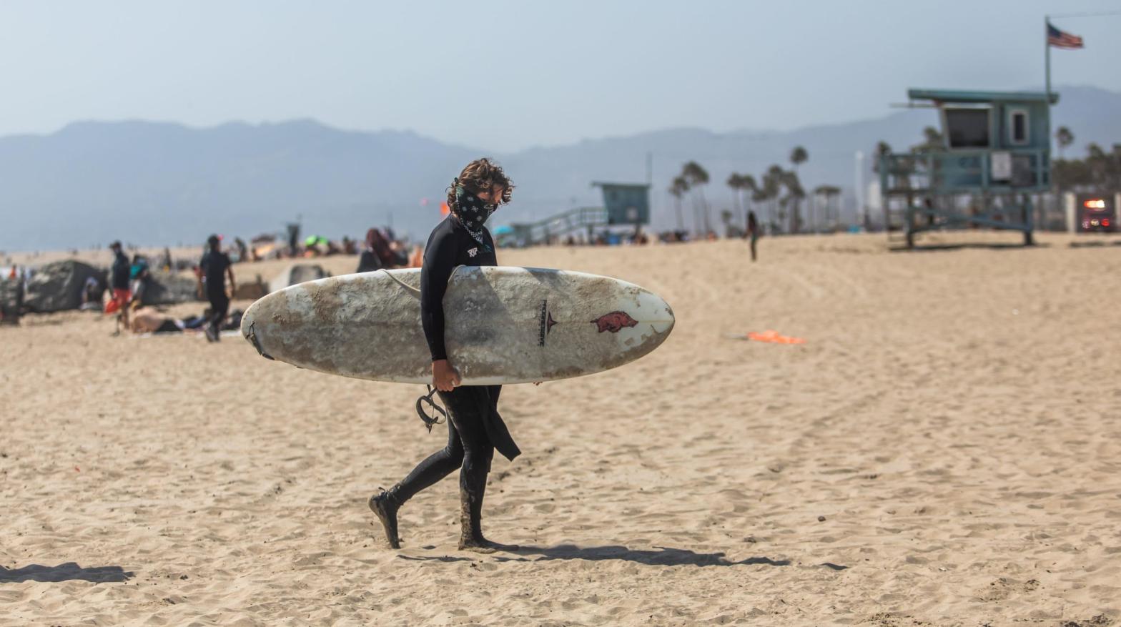 A masked surfer walking at Venice Beach in California during Memorial Day weekend in May. (Photo: Apu Gomes, Getty Images)