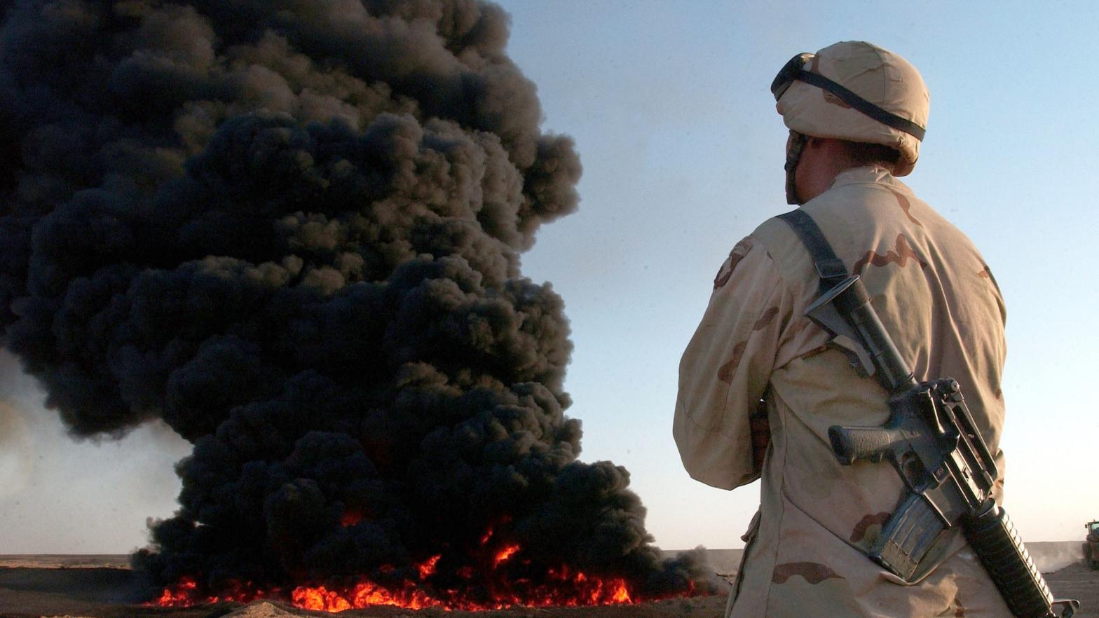 A giant black cloud of burning oil rises behind a U.S. Army soldier in August 2003. (Photo: Scott Nelson, Getty Images)