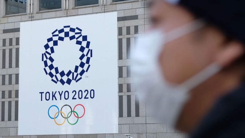 A man wearing a face mask walks by a sign announcing the Tokyo Olympics in March 2020. (Photo: Kazuhiro Nogi / AFP, Getty Images)