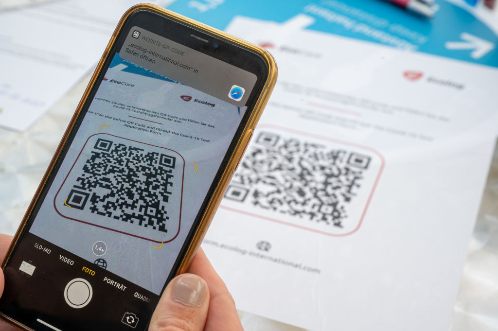 13 August 2020, Bavaria, Munich: A woman scans a digital QR code with her smartphone to register for the corona test at the airport. Photo: Peter Kneffel/dpa (Photo by Peter Kneffel/picture alliance via Getty Images)