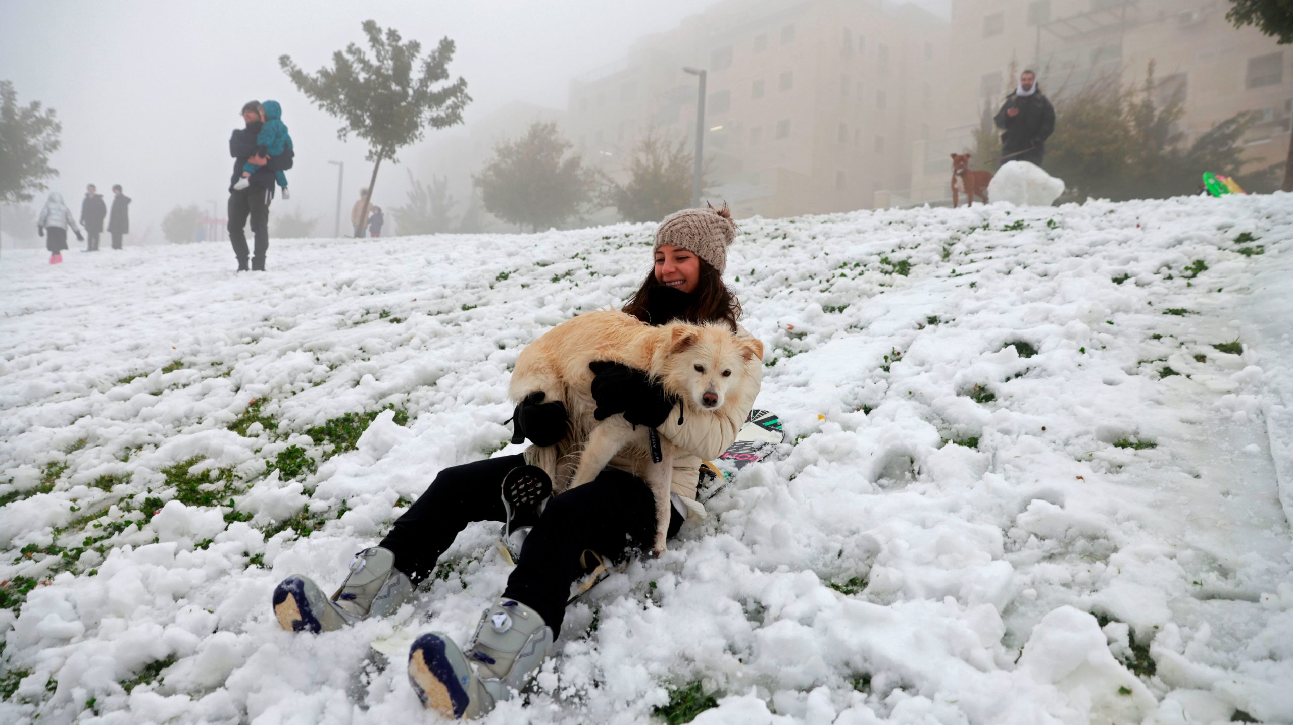 A woman holding a dog slides down a snow-covered slope following a snowstorm in Jerusalem, on Feb. 18, 2021. (Photo: MENAHEM KAHANA, Getty Images)