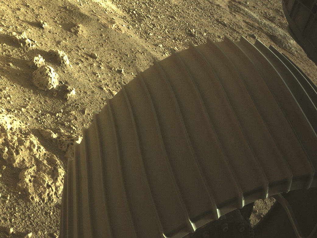 Perseverance's front right wheel, with curious rocks in the background.  (Image: NASA/JPL)