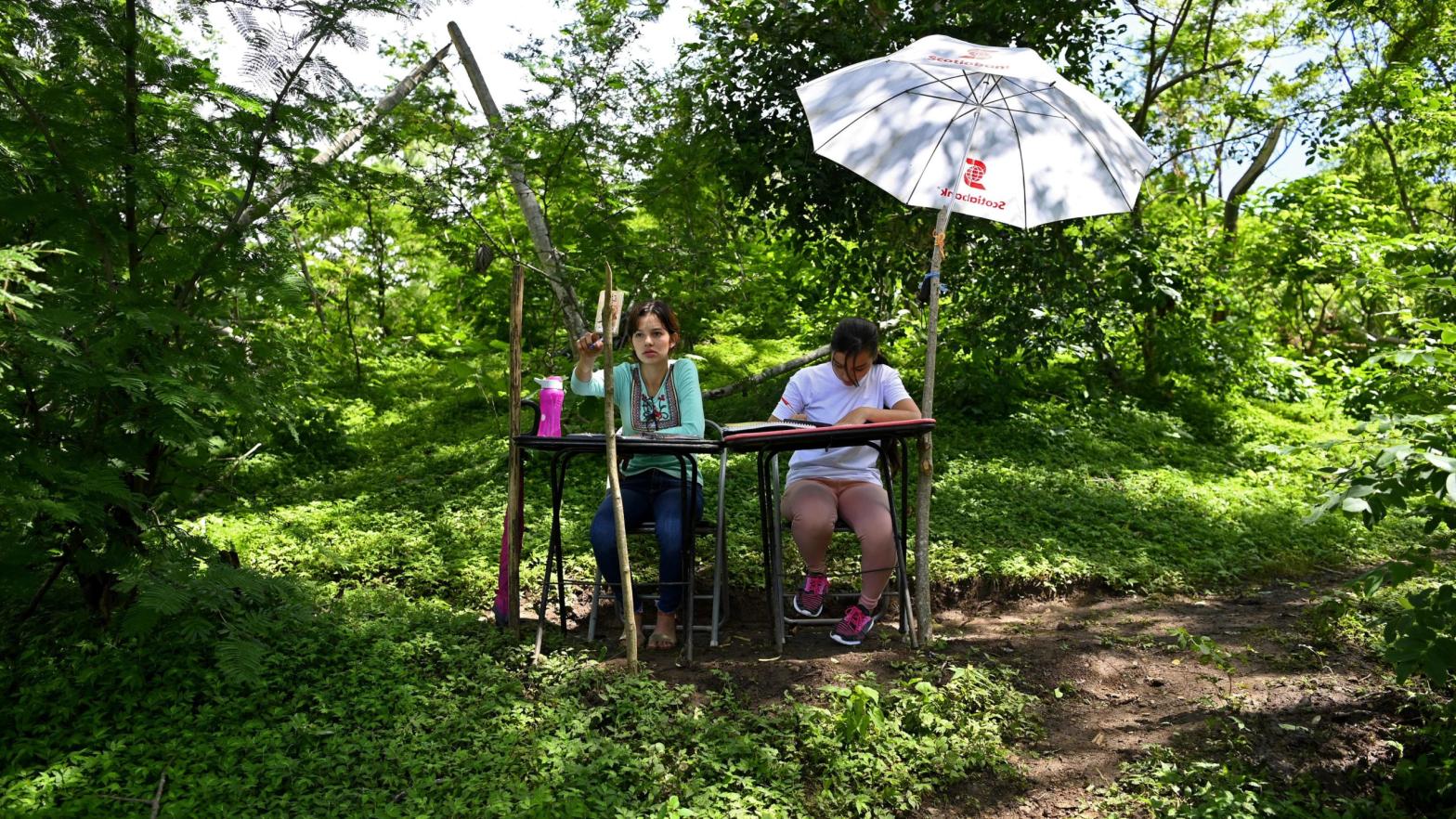 Sisters and university students, Matilde (L) and Marlene Pimentel, do their schoolwork from a hilltop where they can reach internet signal in El Tigre, El Salvador, on August 21, 2020. (Photo: Marvin Recinos/AFP, Getty Images)