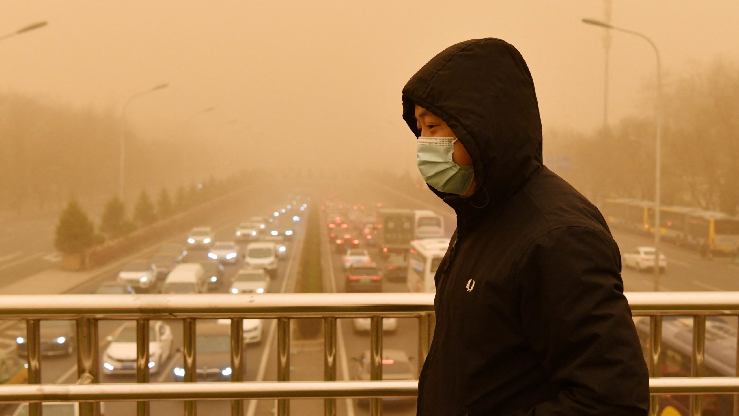 A man walks on a pedestrian overbridge during a sandstorm in Beijing as traffic crawls in the background on March 15, 2021. (Photo: Greg Baker/AFP, Getty Images)