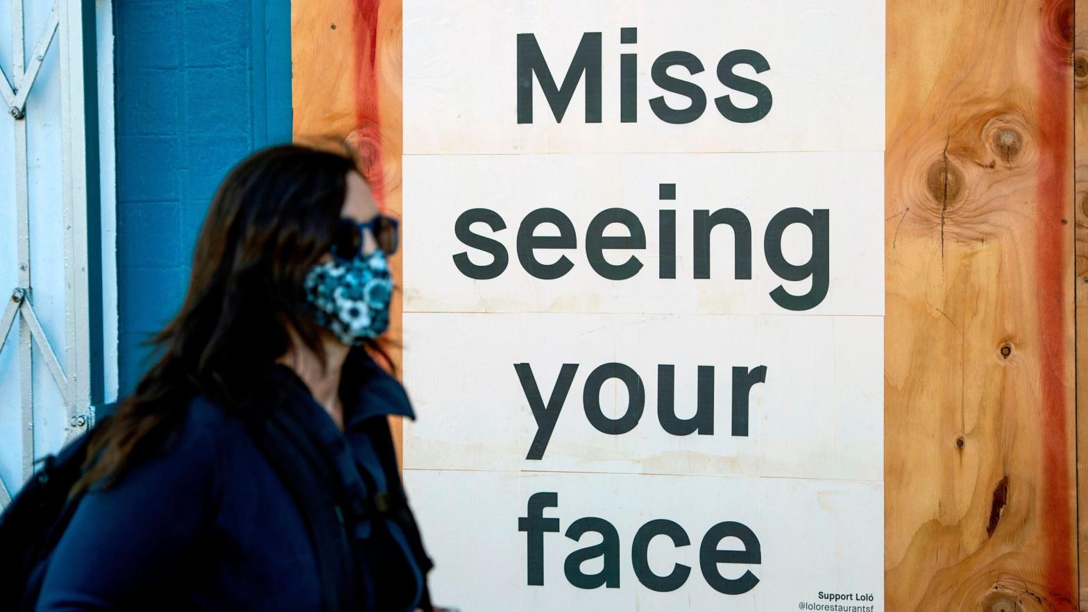 A woman in a face mask walks by a sign posted on a boarded up restaurant in San Francisco, California on April, 1, 2020 (Photo: Josh Edelson/AFP, Getty Images)