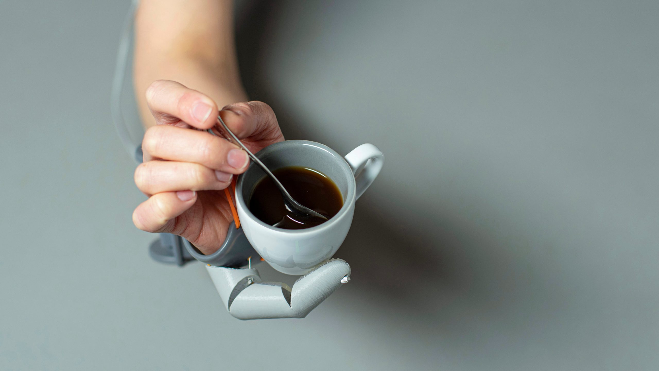A person supporting a coffee cup with the Third Thumb, while stirring a spoon with their natural fingers. (Image: Dani Clode)