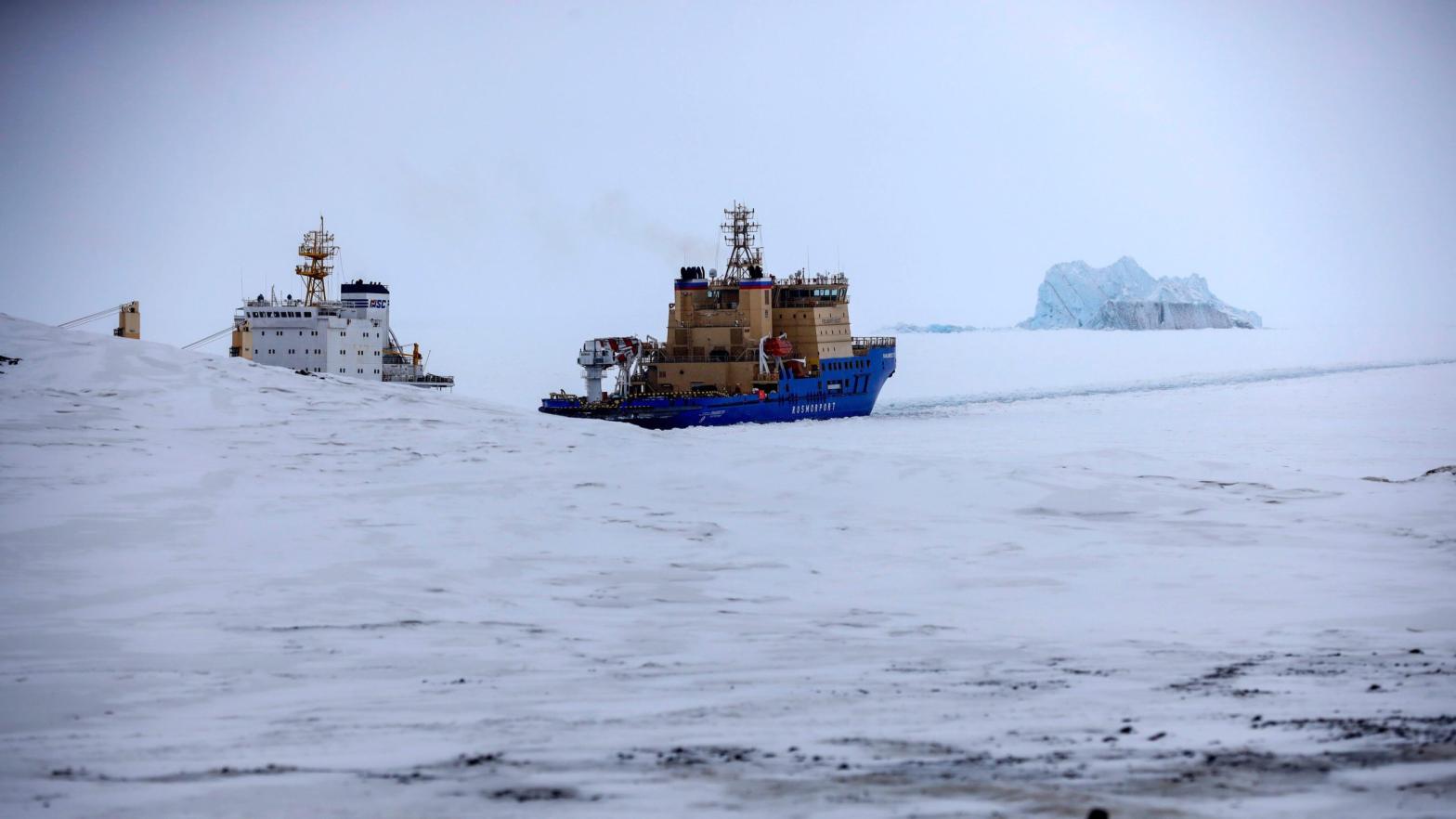 An icebreaker makes the path for a cargo ship with an iceberg in the background near a port on the Alexandra Land island near Nagurskoye, Russia. (Photo: Alexander Zemlianichenko, AP)