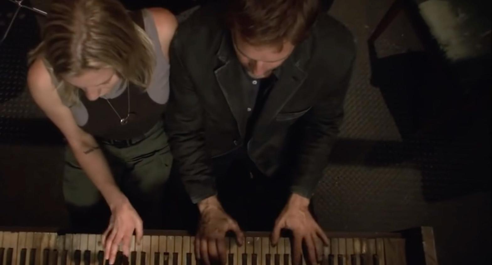 An enigmatic stranger (Roark Critchlow) gives Starbuck (Katee Sackhoff) a piano lesson. (Screenshot: NBCUniversal)