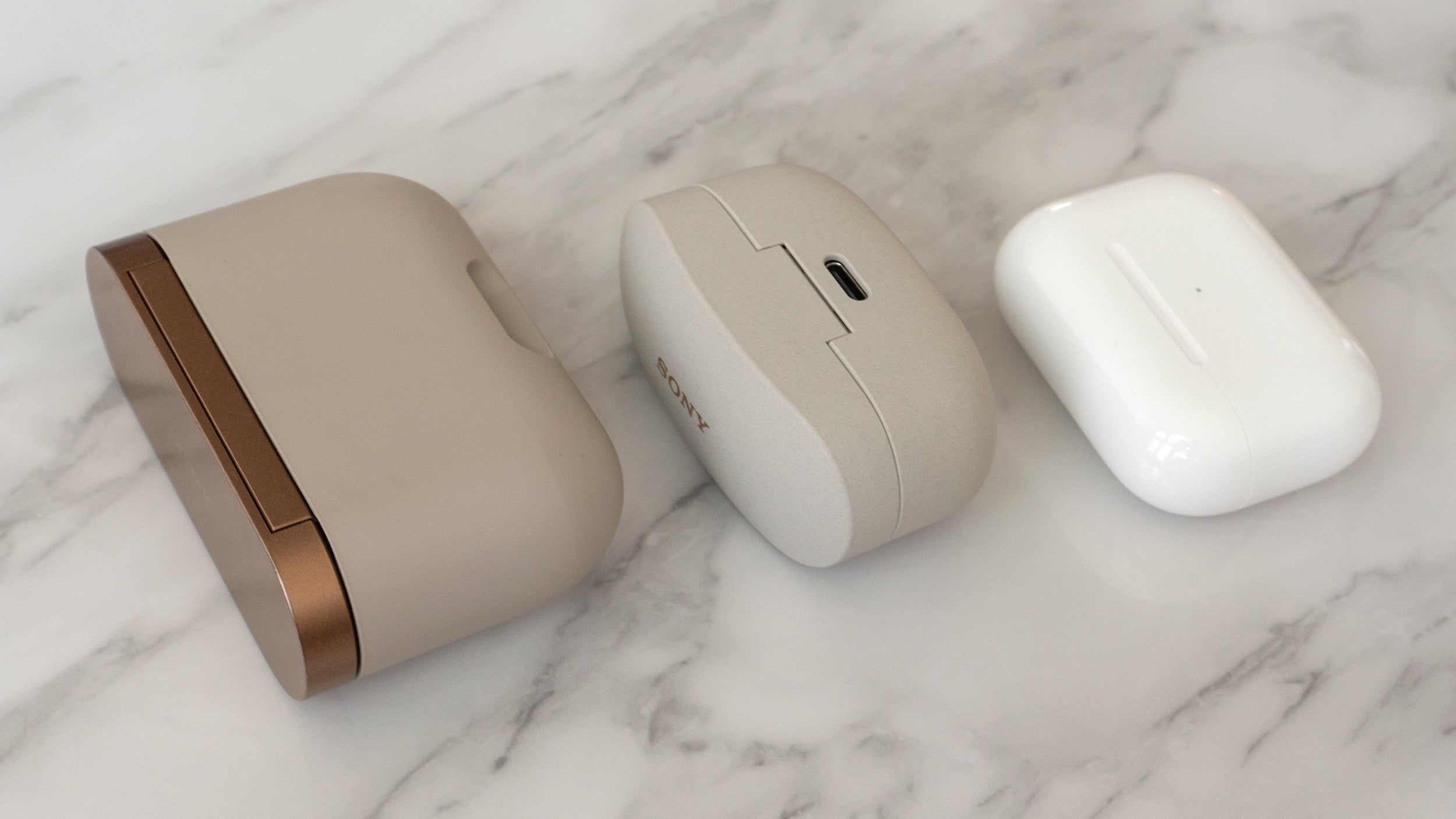 The charging case for Sony's WF-1000XM3 earbuds was an absolute beast (left) and while the charging case for the Sony WF-1000XM4 earbuds is about half the size (centre), it's still not quite as small and pocketable as the AirPods Pro charging case (right). (Photo: Andrew Liszewski/Gizmodo)