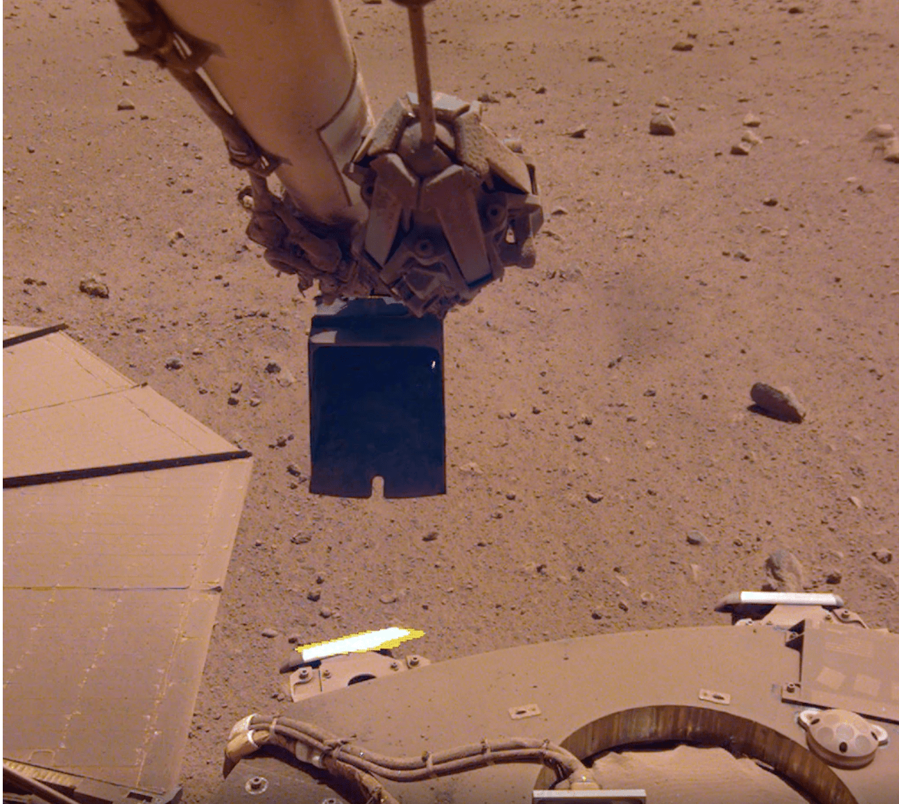InSight's robotic arm attempting to remove dust from the solar panel by sprinkling sand in the wind. (Image: NASA/JPL-Caltech)