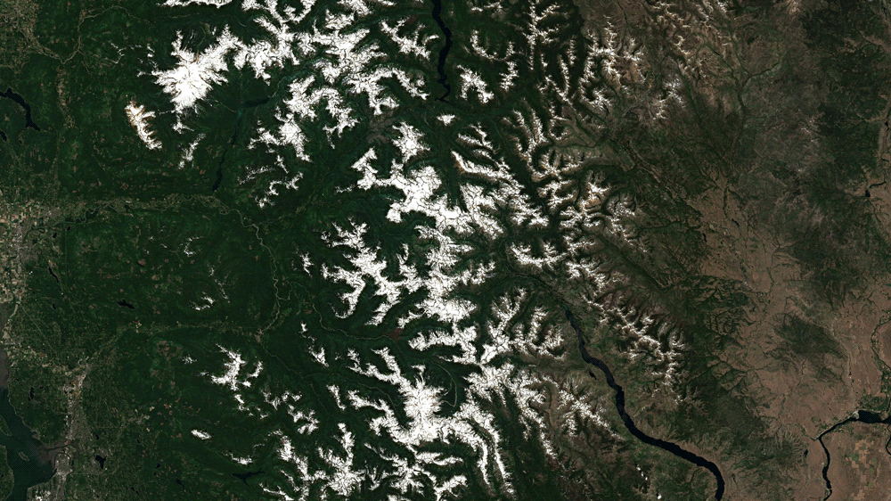 A satellite composite showing the North Cascades on June 26, 2021 and July 11, 2021. A wildfire is also visible. (Gif: Brian Kahn/Sentinel Hub)
