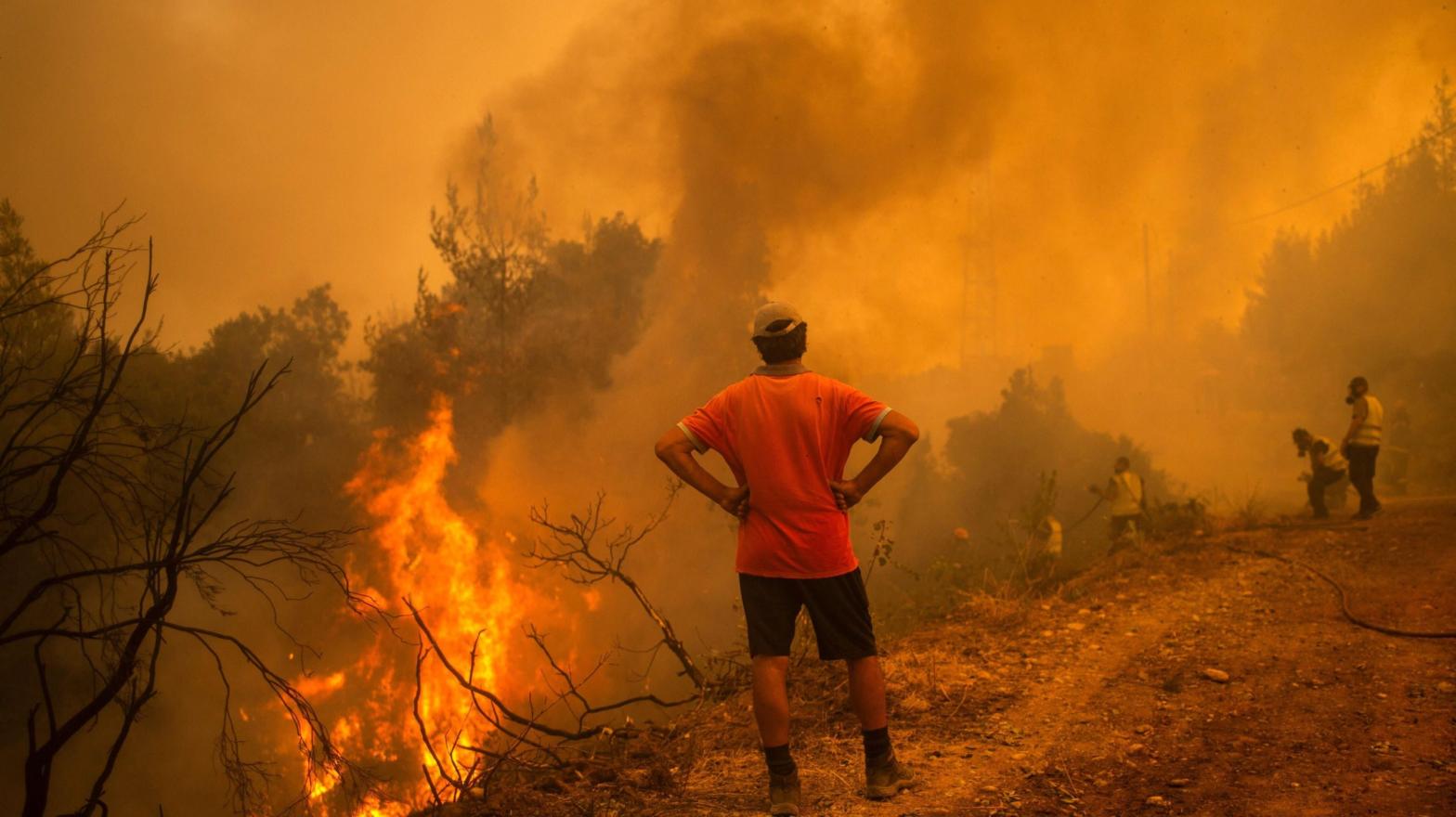 A volunteer watches as firefighters use a water hose to extinguish the blaze of a forest fire in the village of Glatsona on Evia (Euboea) island, on August 9, 2021.  (Photo: ANGELOS TZORTZINIS, Getty Images)