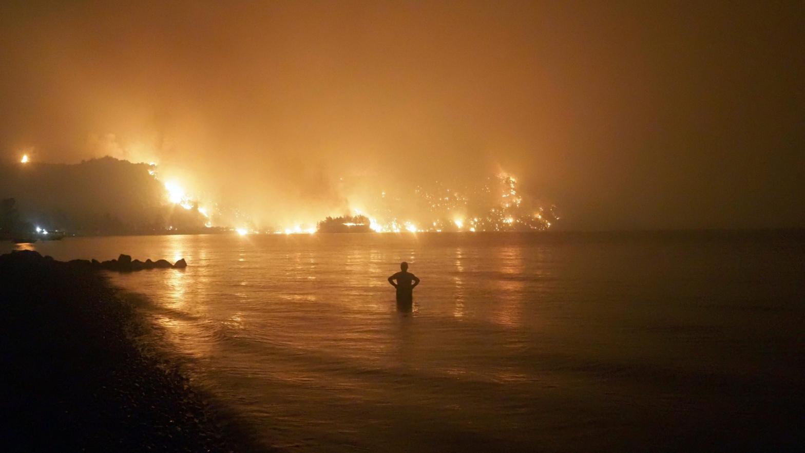 A man watches the flames as wildfire approaches Kochyli beach near Limni village on the island of Evia, late Friday, Aug. 6, 2021. (Photo: Thodoris Nikolaou, AP)
