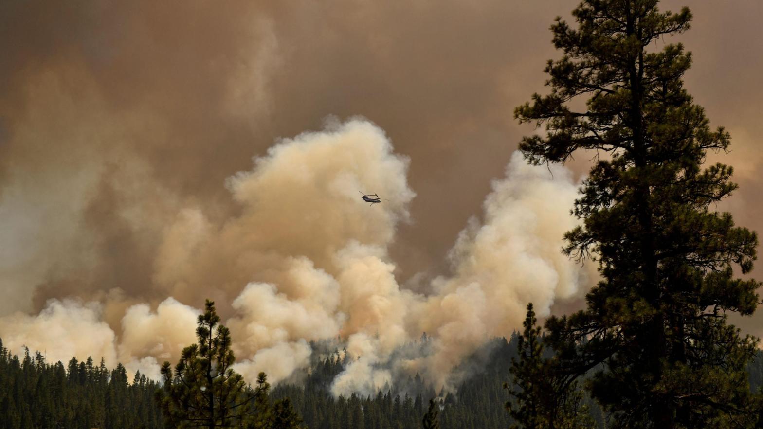 A firefighting helicopter flies past smoke plumes after making a water drop during the Dixie Fire. (Photo: Patrick T. Fallon/AFP, Getty Images)