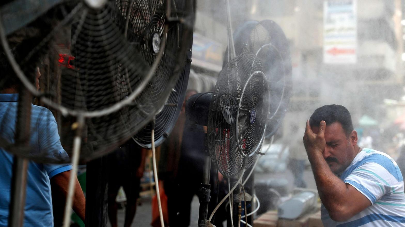 A man stands by fans spraying air mixed with water vapour deployed by donors to cool down pedestrians along a street in Iraq's capital Baghdad on June 30, 2021 amidst a severe heat wave. (Photo: Ahmad Al-Rubaye/AFP, Getty Images)