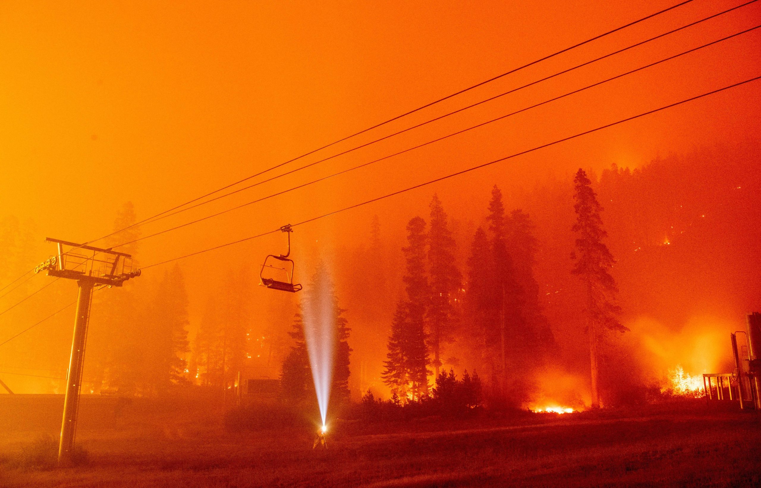 A photographer shines a flashlight towards a chair lift as flames surround Sierra-at-Tahoe Resort, a skiing area, during the Caldor fire in Twin Bridges, California, on Aug. 30, 2021 (Photo: Josh Edelson/AFP, Getty Images)