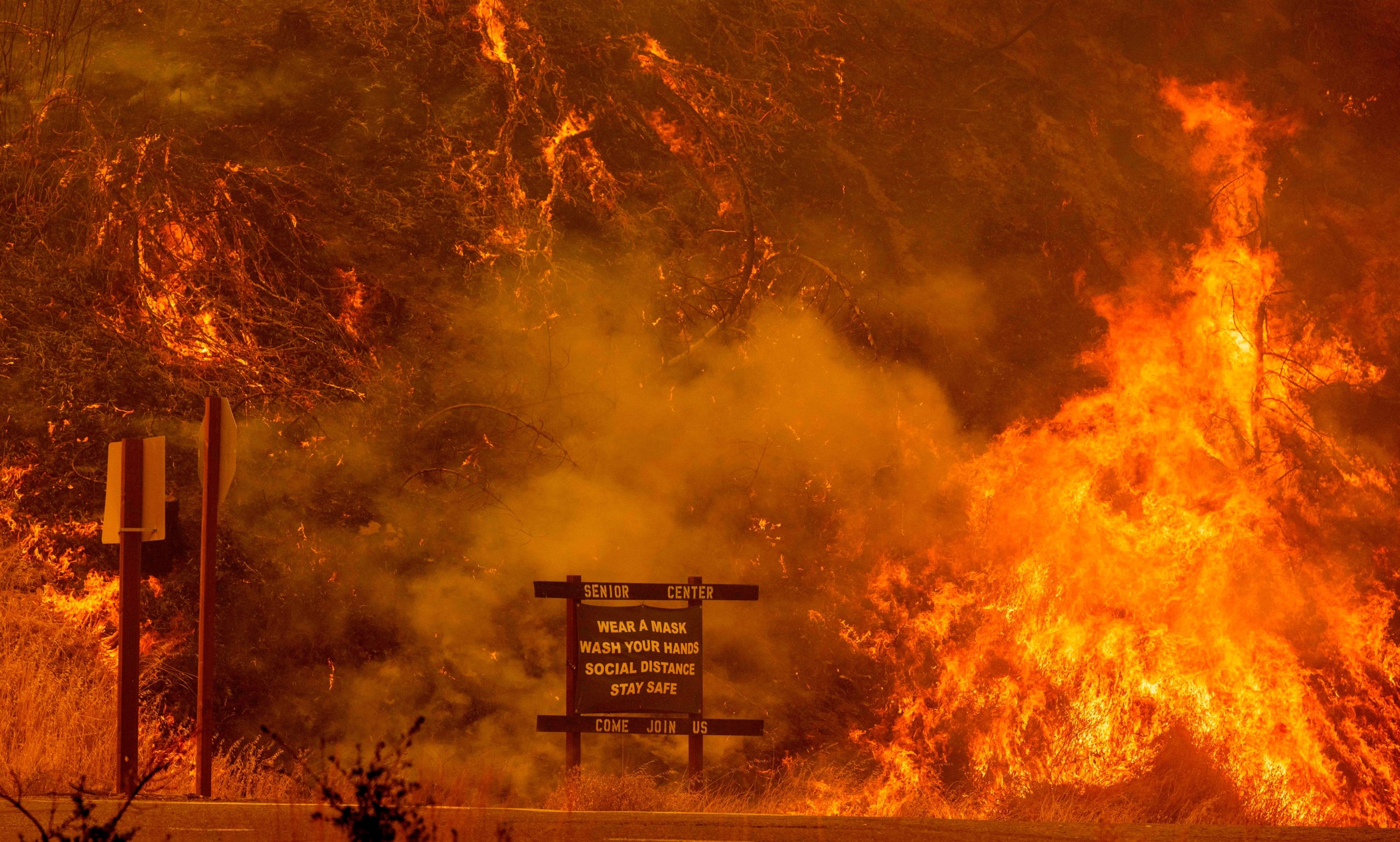 A sign warning people about Covid-19 is surrounded by flames during the Hennessey Fire near Lake Berryessa in Napa, California,, on Aug. 18, 2020. (Photo: Josh Edelson/AFP, Getty Images)