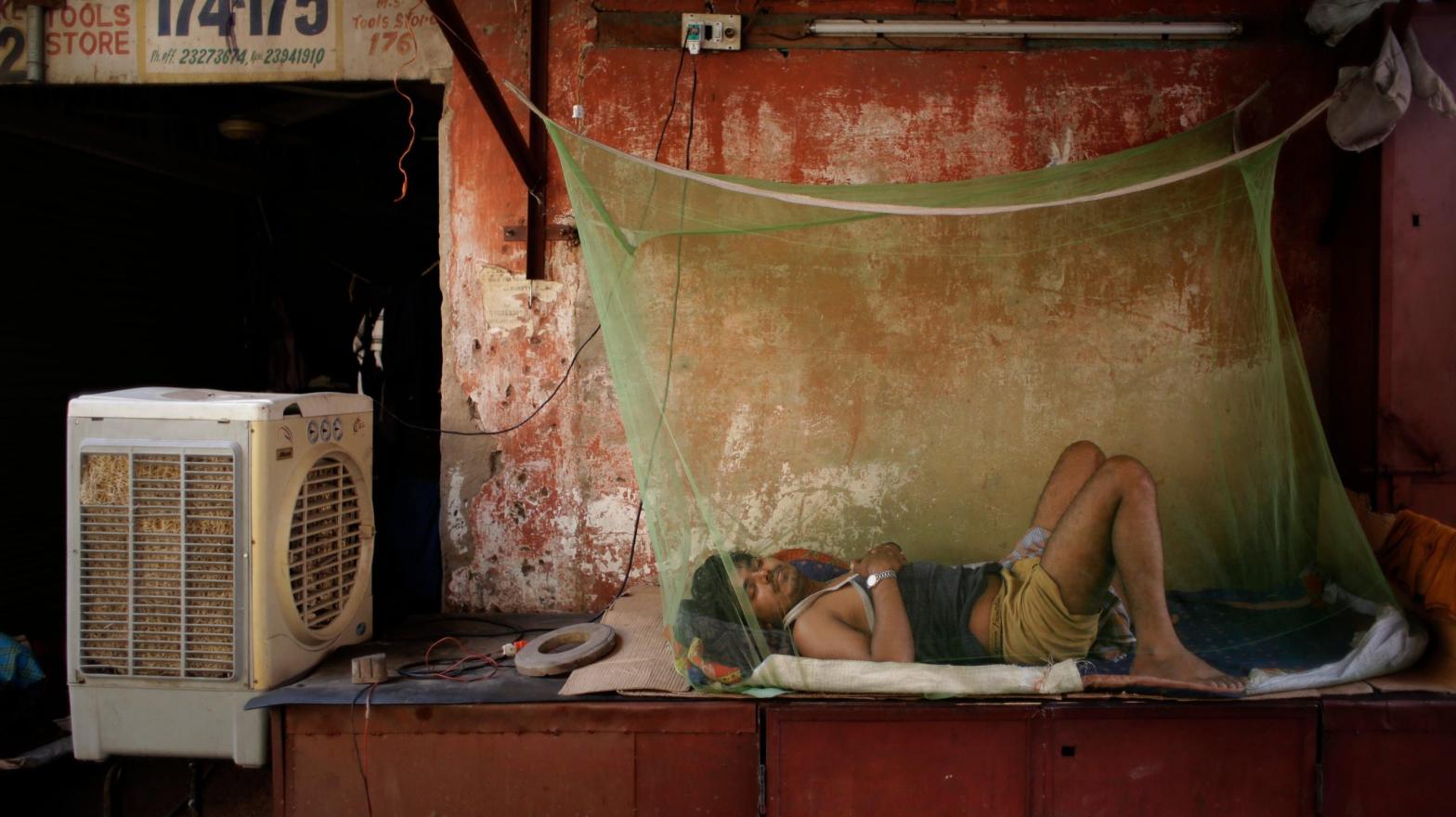 An Indian migrant daily wage worker sleeps next to an air cooler under a mosquito net on a steel box, used to store items of shop at night, in New Delhi. (Photo: Altaf Qadri, AP)