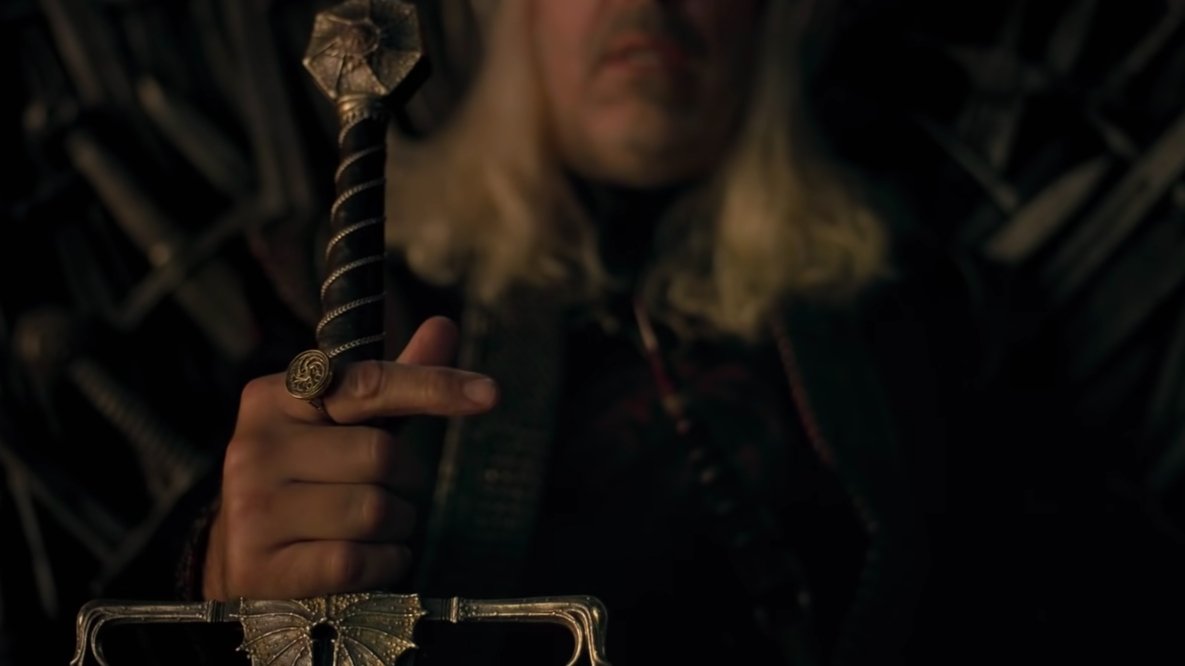 King Viserys shows off his sword and Targaryen sigil ring while sitting on the Iron Throne. (Screenshot: HBO)