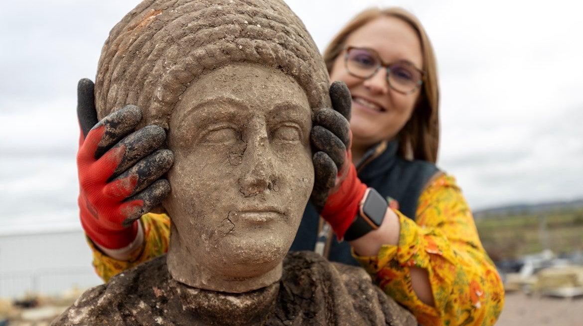 Archaeologist Rachel Wood positioning a stone bust atop its corresponding torso.  (Image: HS2)