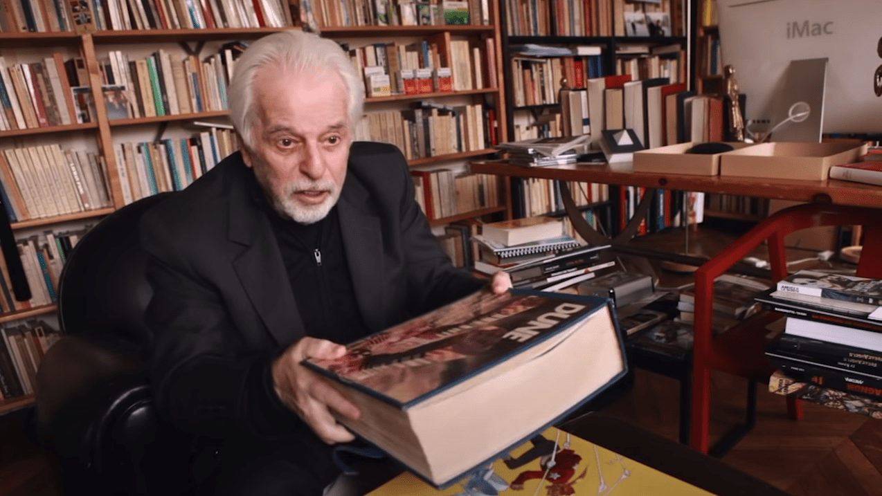 Alejandro Jodorowsky and a copy of his Dune book, one of which is going up for auction. (Screenshot: YouTube, Fair Use)