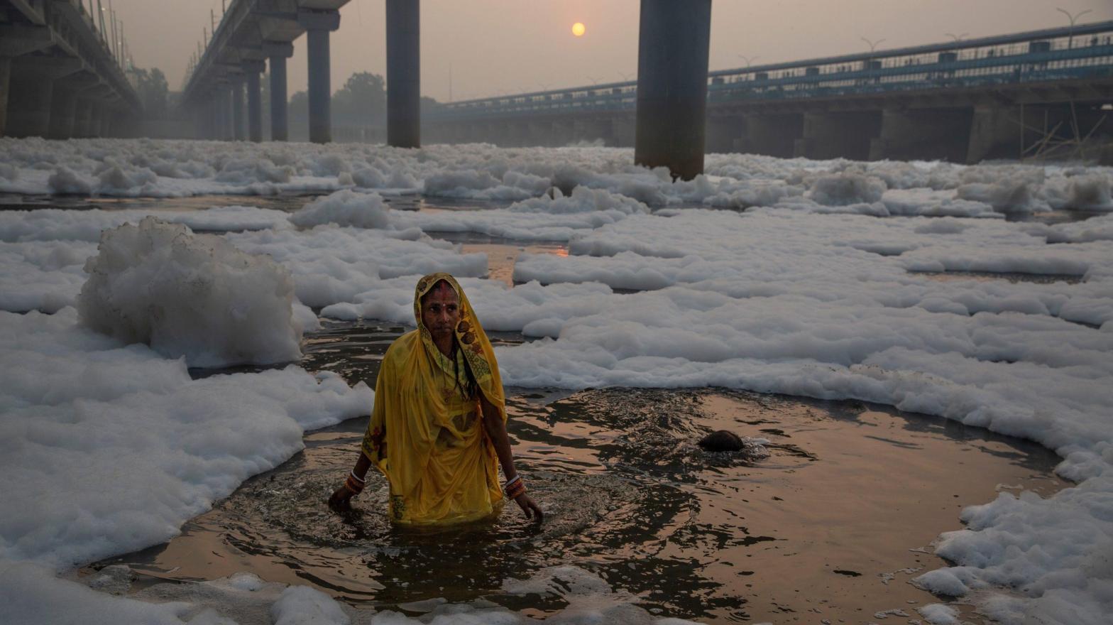 A woman wades into the Yamuna river, covered by chemical foam caused due to industrial and domestic pollution, during Chhath Puja festival. (Photo: Altaf Qadri, AP)