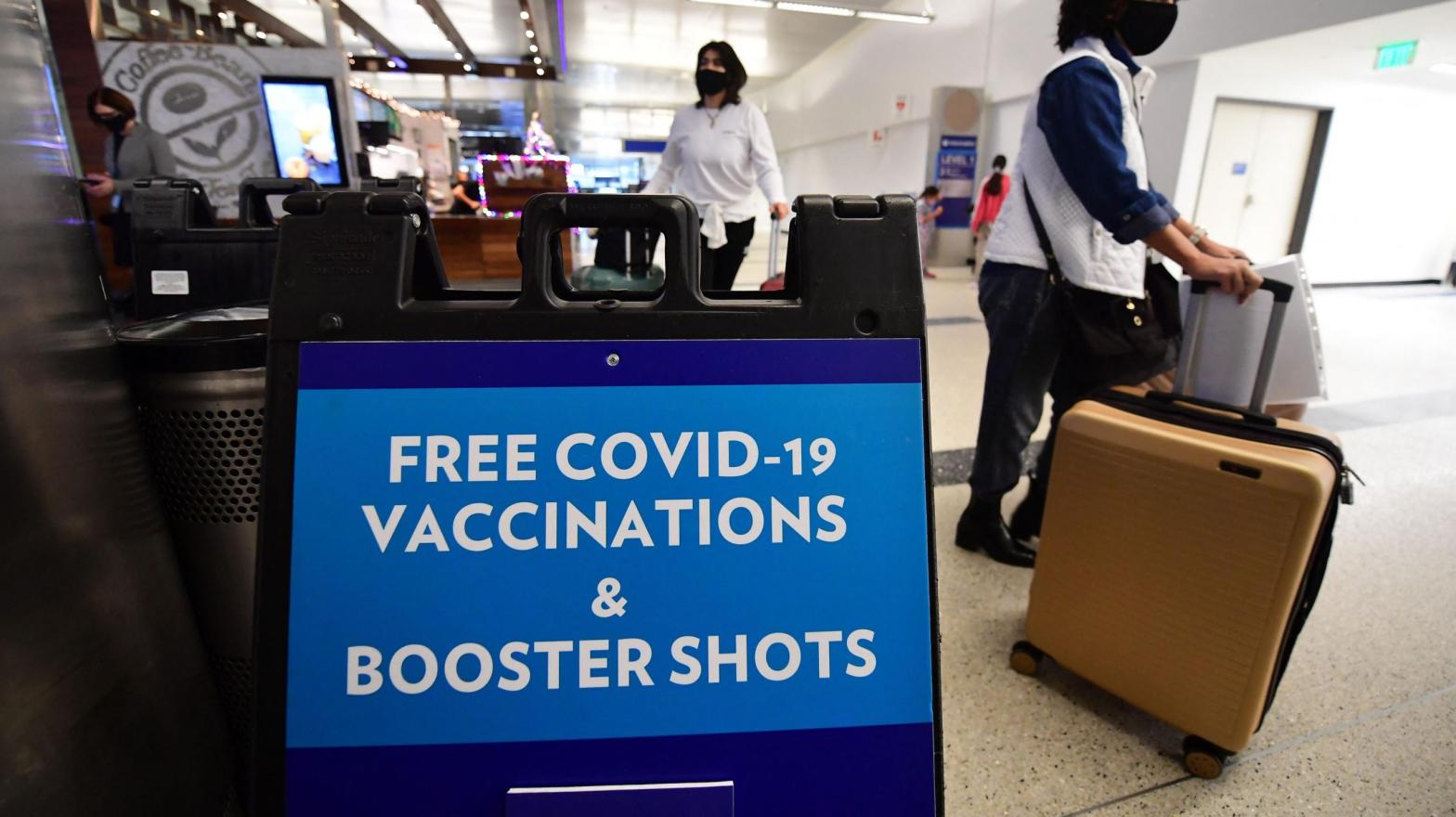 Travellers walk past a sign offering free Covid-19 vaccinations and booster shots at a pop-up clinic in the international arrivals area of Los Angeles International Airport in Los Angeles, California on December 22, 2021. (Image: Frederic J. Brown/AFP, Getty Images)