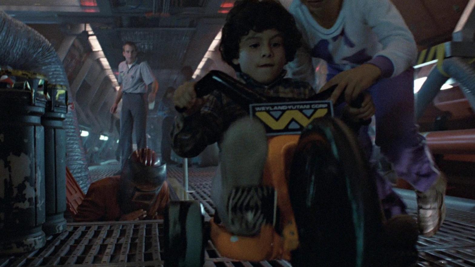A kid rides a Weyland-Yutani-branded Big Wheel in this deleted scene from Aliens. (Screenshot: 20th Century)