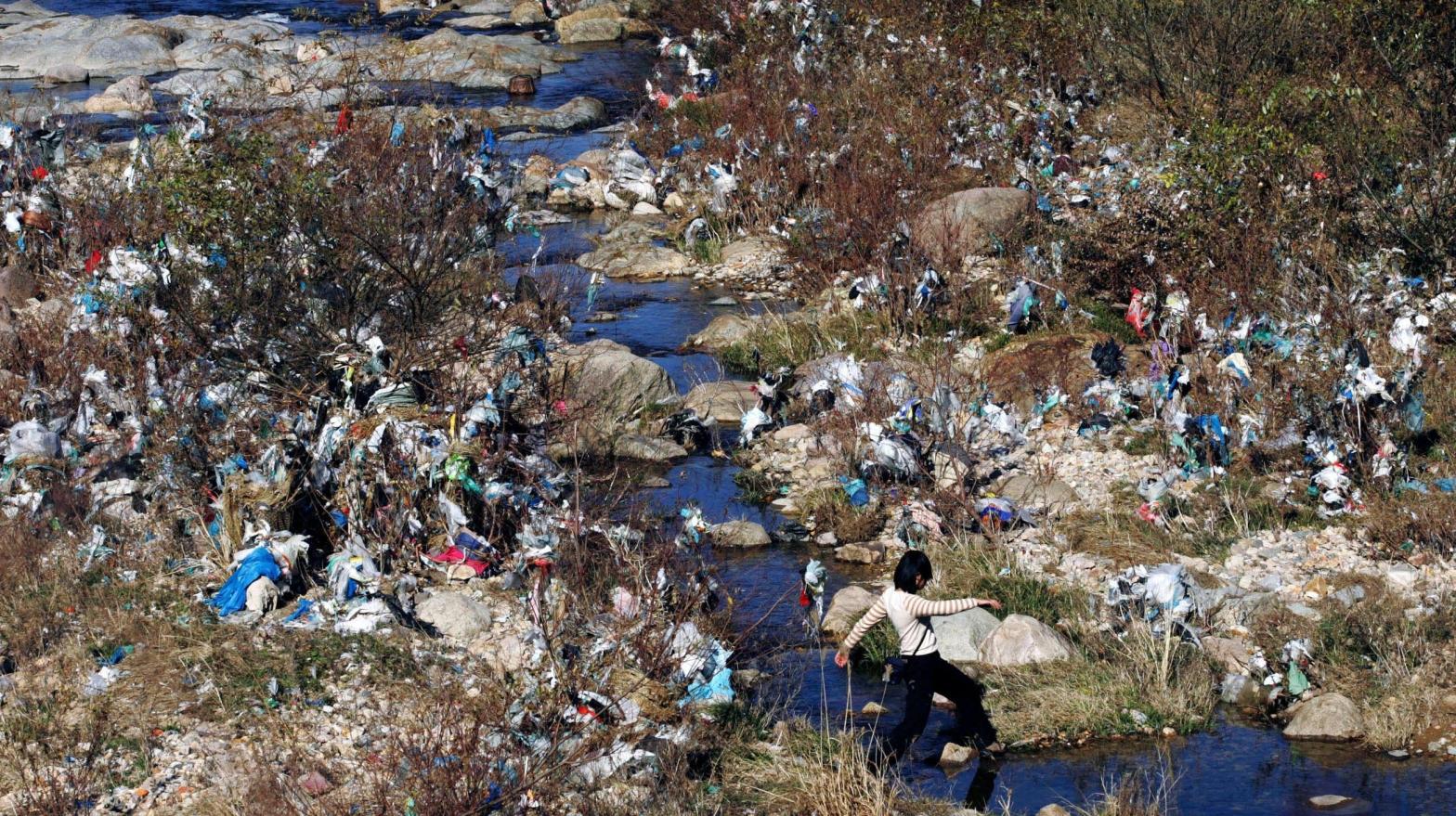 A woman crosses a stream running through land littered with plastic wastes in Shangxi village, eastern China's Zhejiang province. (Photo: CHINATOPIX, AP)