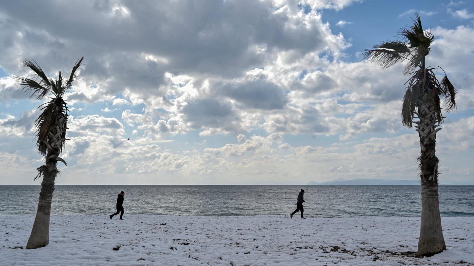 People walk along a snow-covered beach in Athens on January 25, 2022. (Photo: Louisa Gouliamaki/AFP, Getty Images)