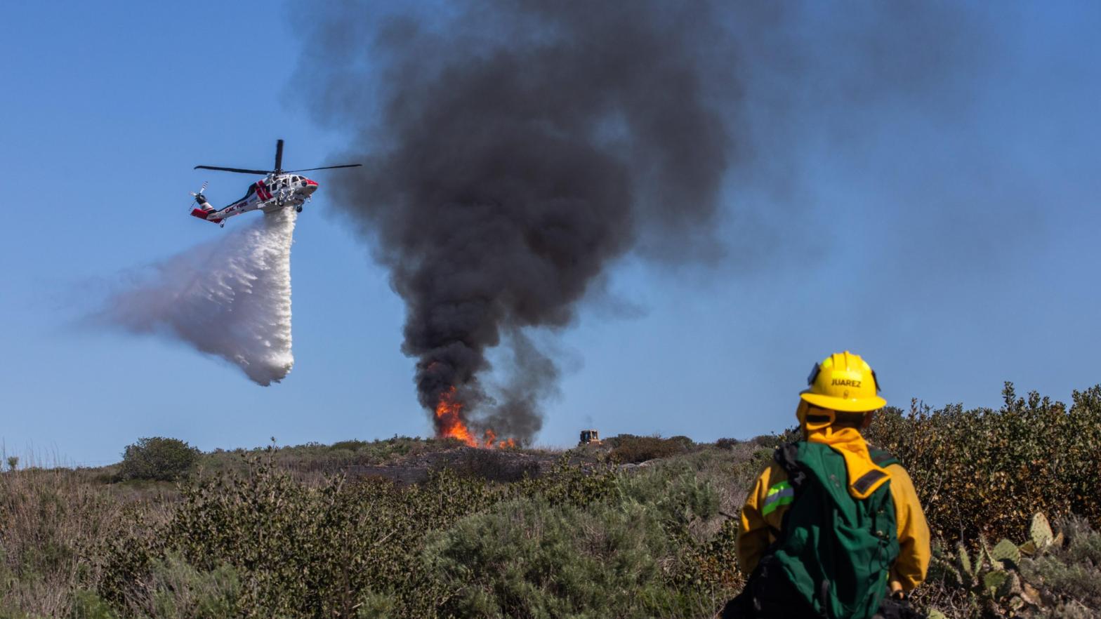 A firefighter watches as a helicopter drops water on a smouldering hillside on February 10, 2022 in Laguna Beach, California. (Photo: Apu Gomes, Getty Images)