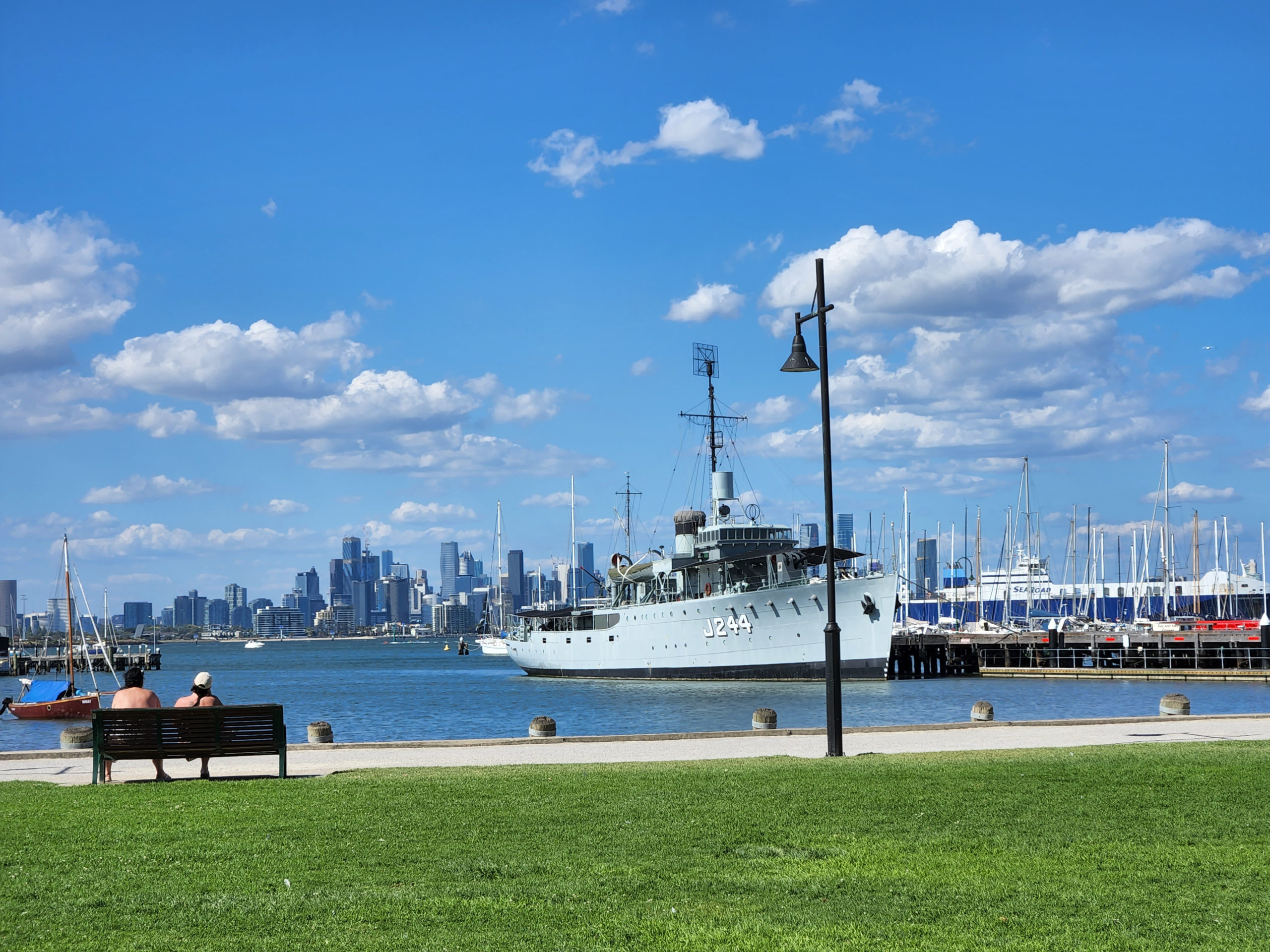 A navy ship on a sunny day with the Melbourne skyline behind it