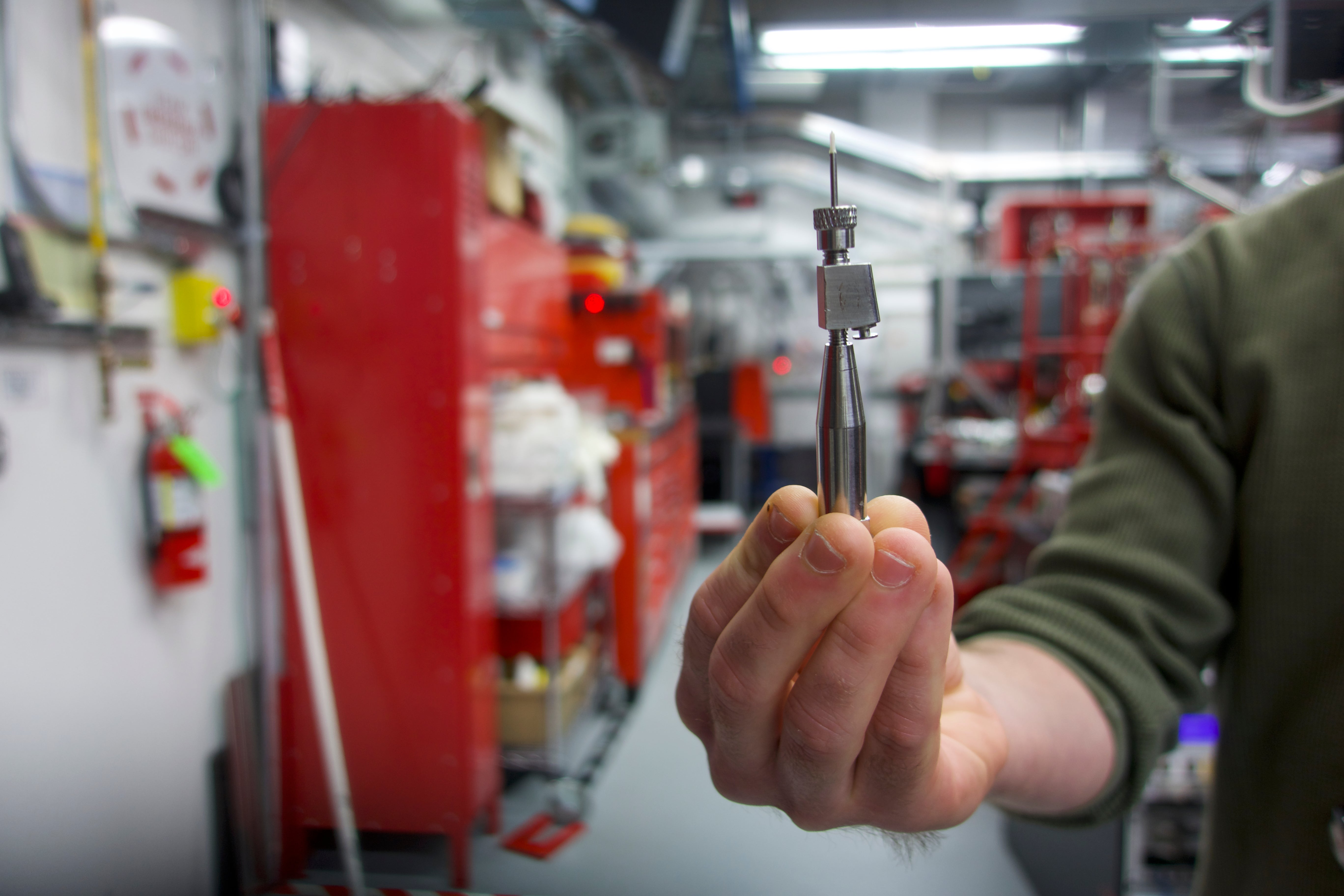 A researcher holds up a needle that emits sample in the Coherent X-ray Imaging instrument. (Photo: Isaac Schultz)