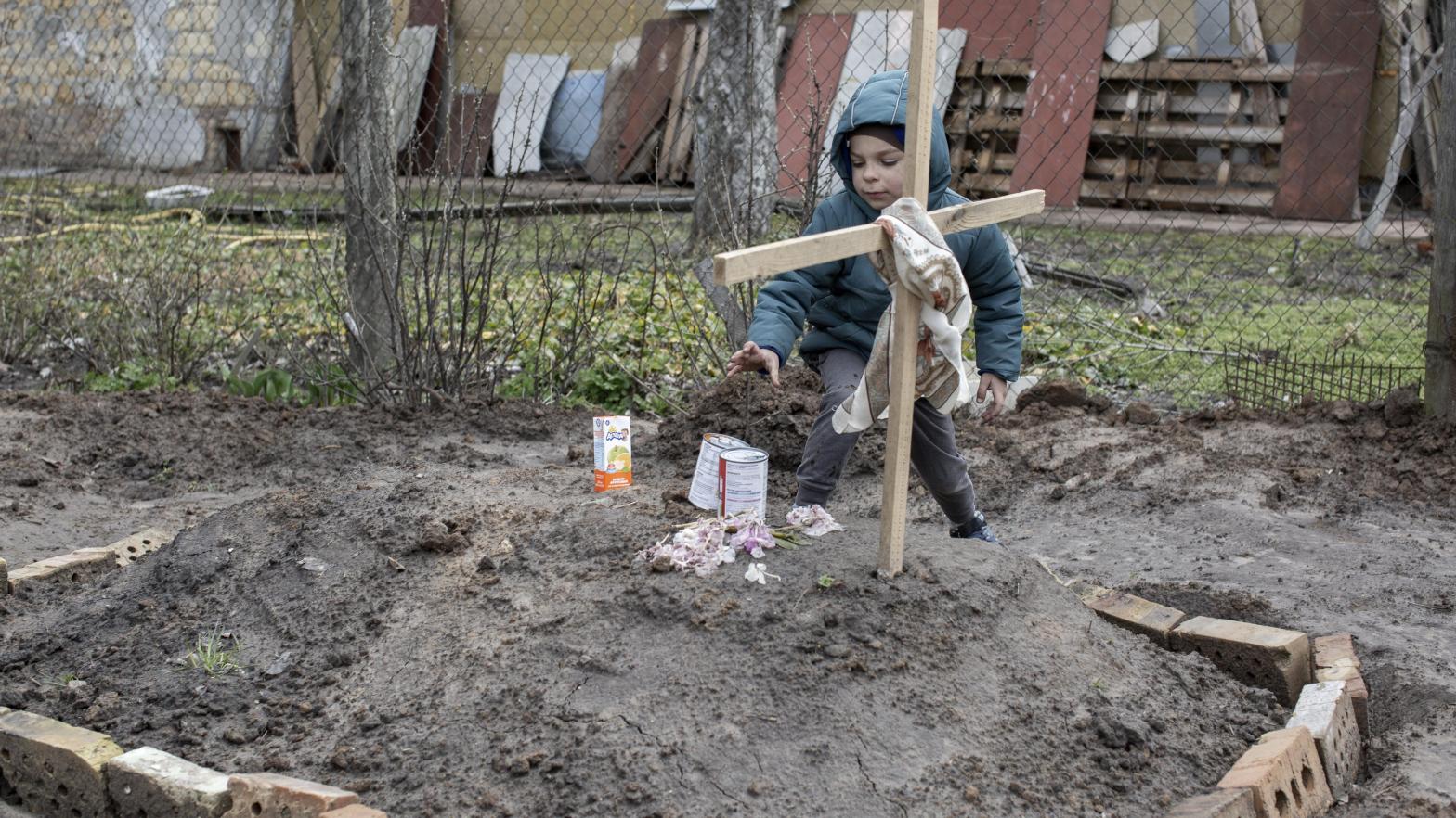A young kid gives an offering of food to the grave of a woman in the town of Bucha, on the outskirts of Kyiv, on April 4, 2022. (Photo: Narciso Contreras/Anadolu Agency, Getty Images)