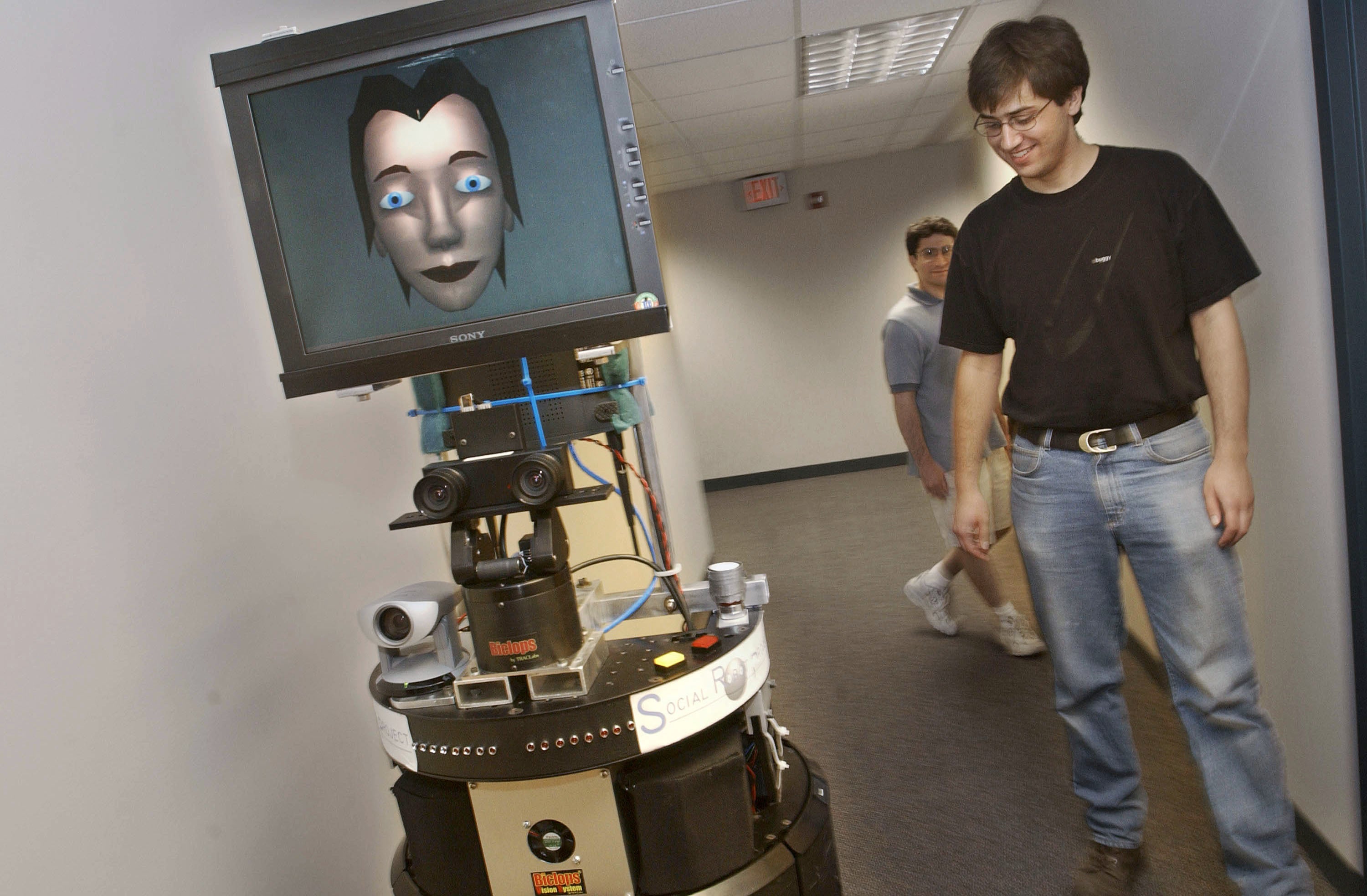 Brennan Sellner (R) and Dani Goldberg, students at Carnegie Mellon  University, watch GRACE, a prototype mobile robot, as it moves down a  hall July 15, 2002 at the Robotics Institute of Carnegie Mellon  University in Pittsburgh, Pennsylvania. (Photo: Chris Hondros, Getty Images)
