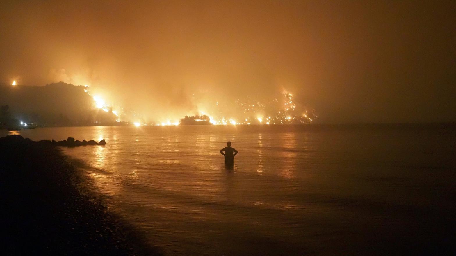 A man watches a wildfire approach the beach in Evia, Greece, in August 2021. (Photo: Thodoris Nikolaou, AP)