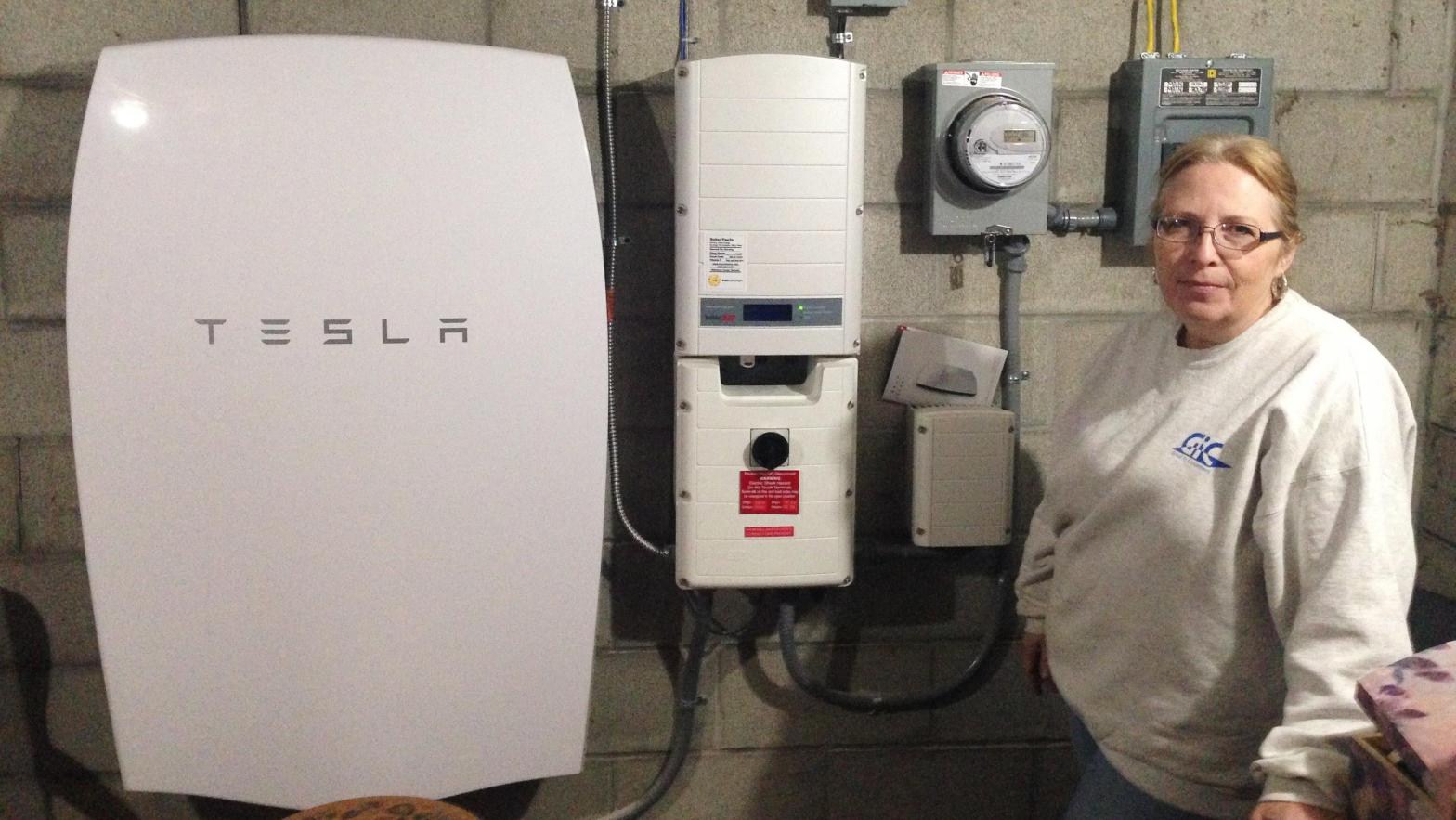 A customer in Vermont stands next to a Tesla Powerwall battery and inverter which she uses to store solar energy. (Photo: Dave Gram, AP)