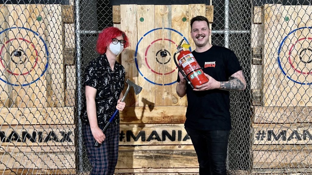 A redheaded person holding an axe and a man holding a fire extinguisher