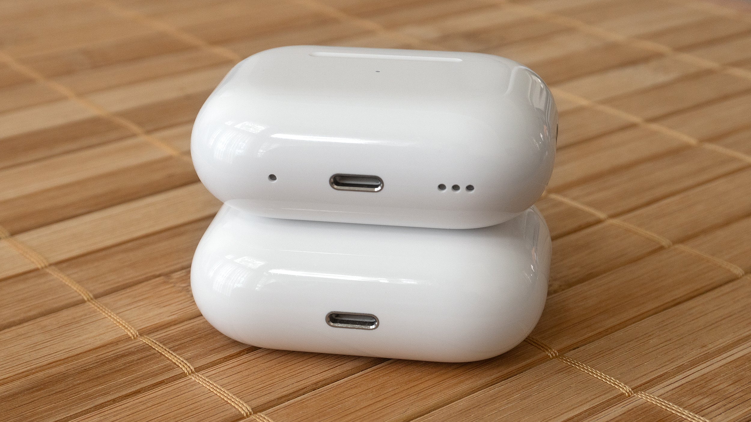 The original AirPods Pro charging case (bottom) compared to the 2nd Gen case (top). They are nearly identical although the new case adds speaker holes and a lanyard loop. (Photo: Andrew Liszewski | Gizmodo)