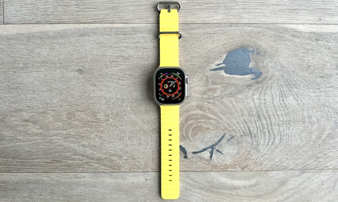 And Apple Watch Ultra with a yellow Ocean band on a wooden floor