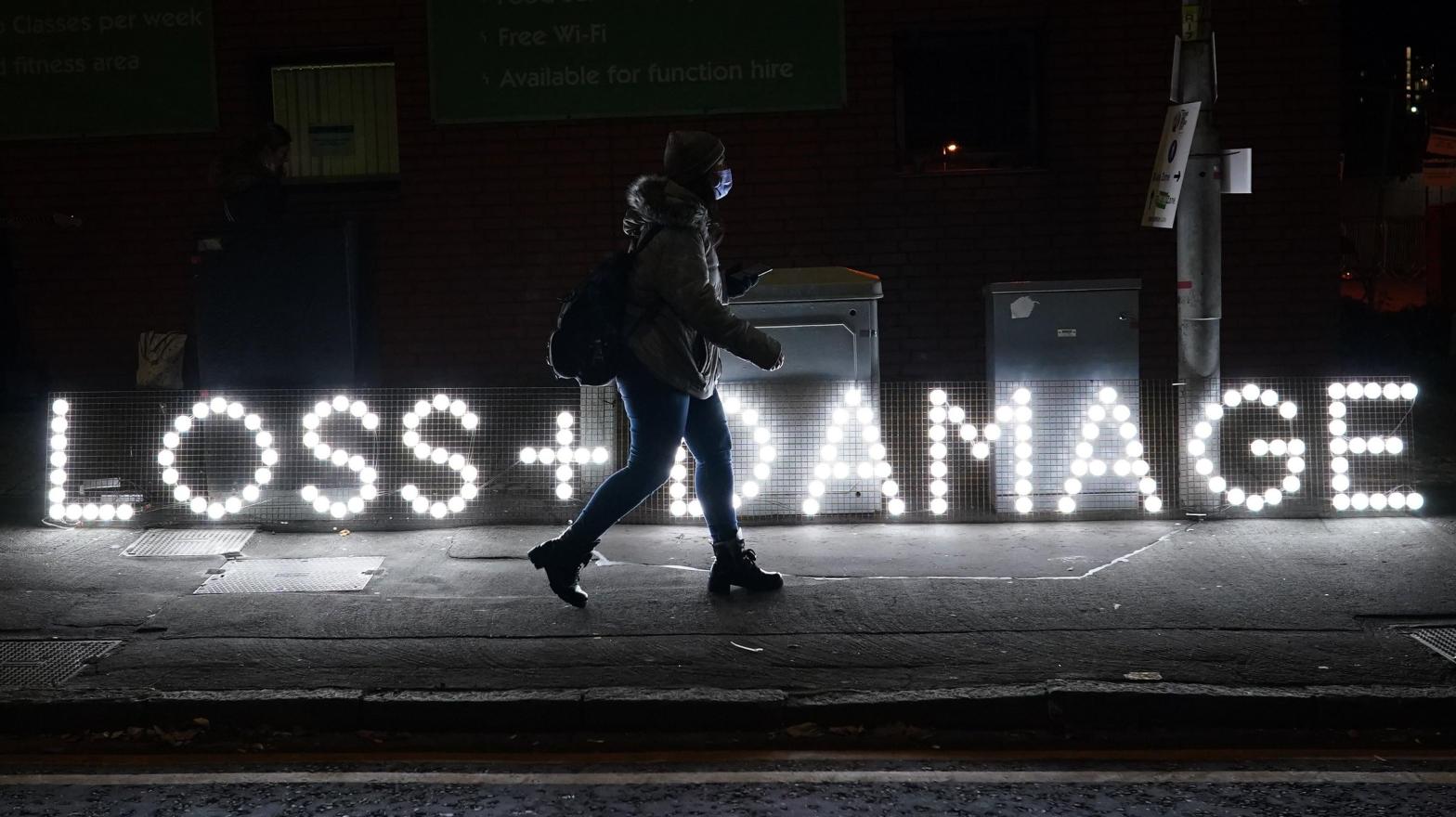 A woman walks by a lit sign in Glasgow on November 4, 2021 at last year's COP. (Photo: Ian Forsyth, Getty Images)