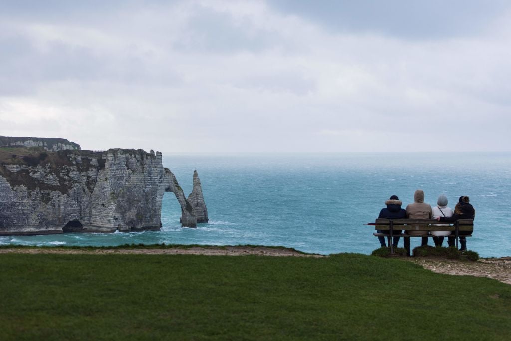 People sit on bench looking at a natural arch and the chalk cliffs in Etretat on January 4, 2022. (Photo: SAMEER AL-DOUMY/AFP, Getty Images)