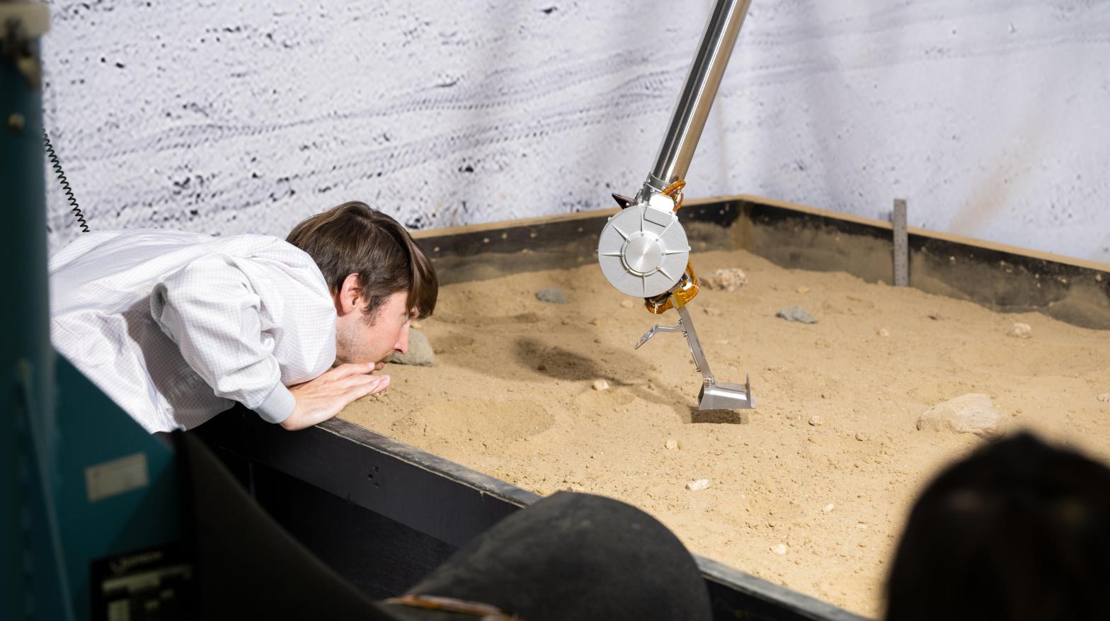 An engineer at NASA's Jet Propulsion Laboratory observes the COLDArm being tested in a bed of simulated lunar soil. (Image: NASA/JPL-Caltech)