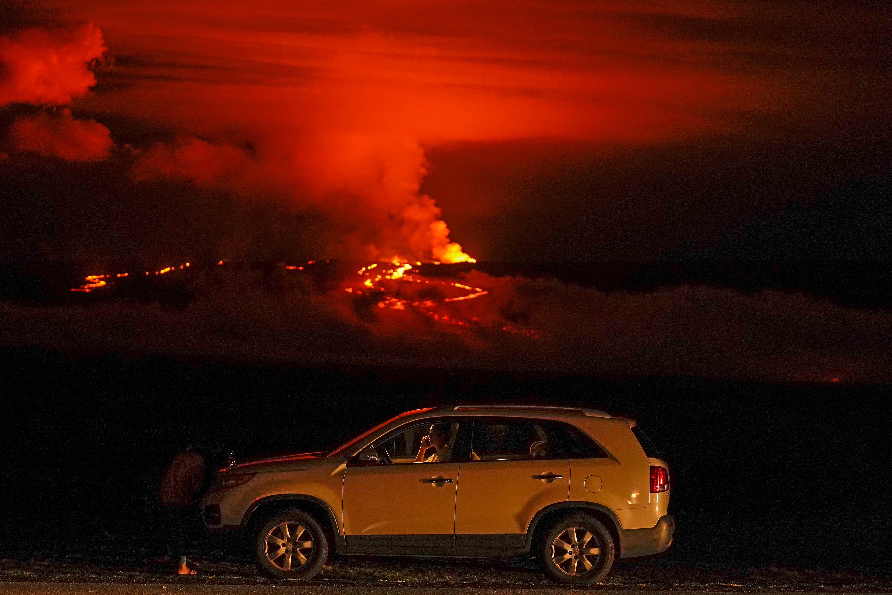 A man talks on a phone in his car alongside Saddle Road as the Mauna Loa volcano erupts Wednesday, Nov. 30, 2022, near Hilo, Hawaii. (Photo: Gregory Bull, AP)
