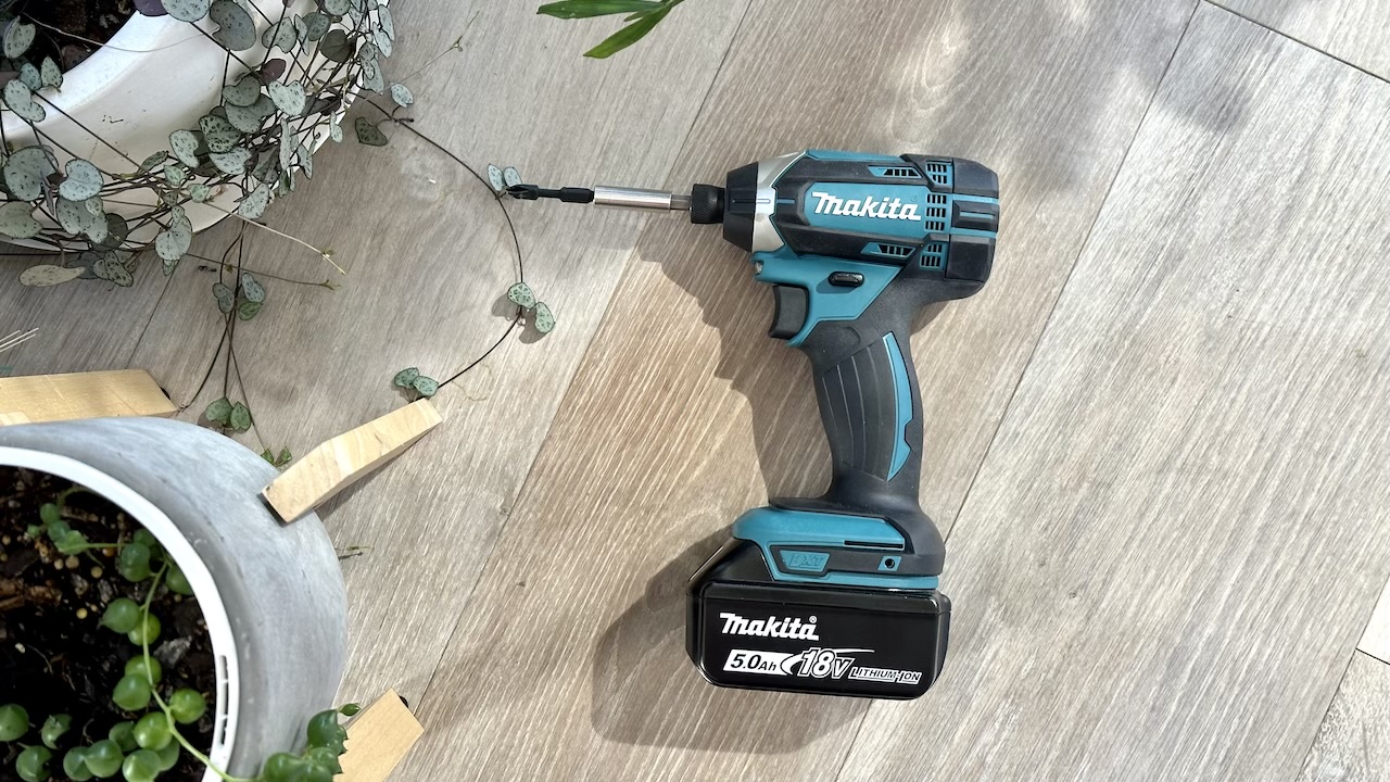Makita cordless drill on a wooden floor surrounded by plants