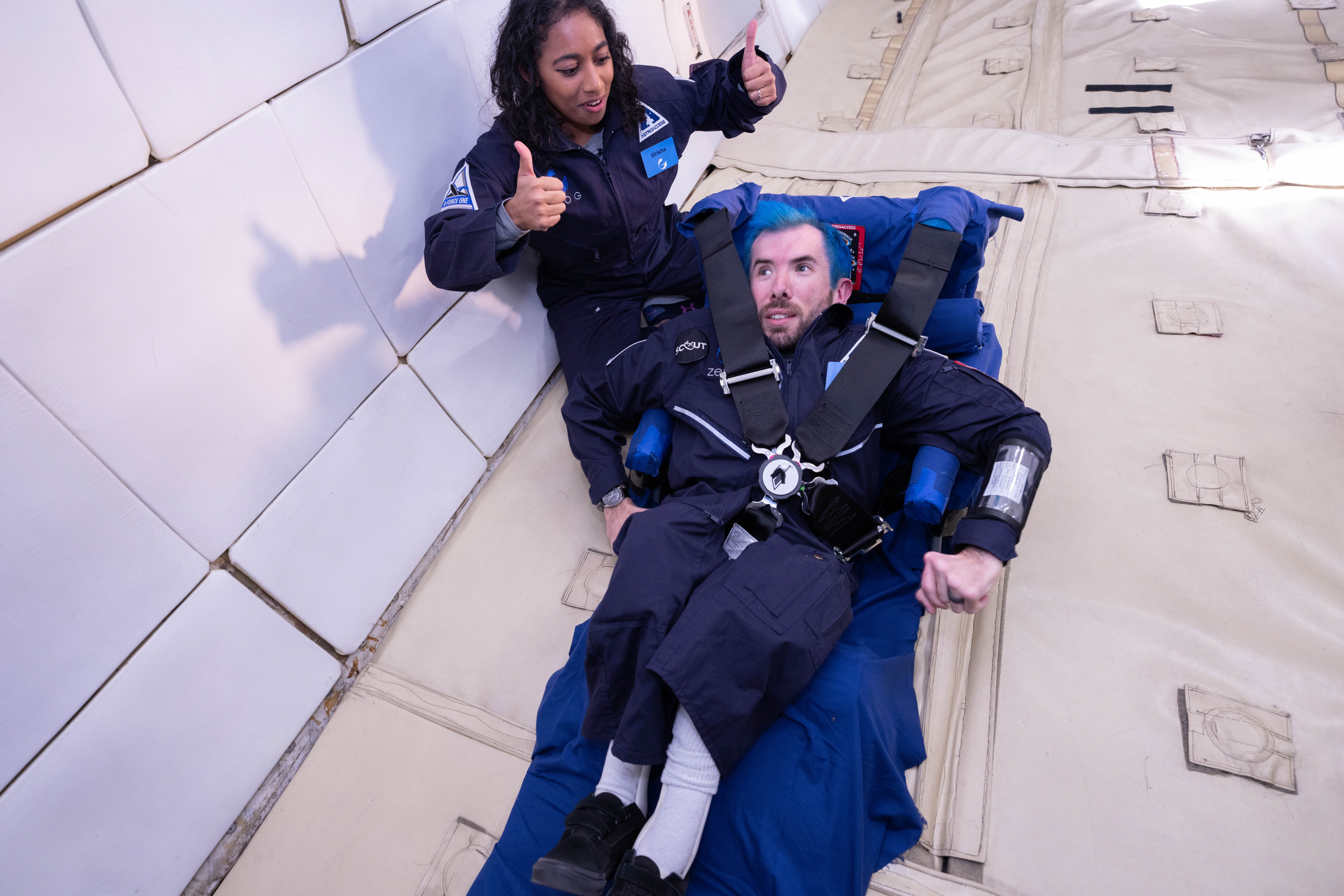 Eric Ingram, a returning flyer from AstroAccess's inaugural 2021 mission, practices getting in and out of a 5-point harness attached to a simulated space capsule seat. He is joined by astronaut and aerospace executive Sirisha Bandla.  (Photo: Tasha Dixon)