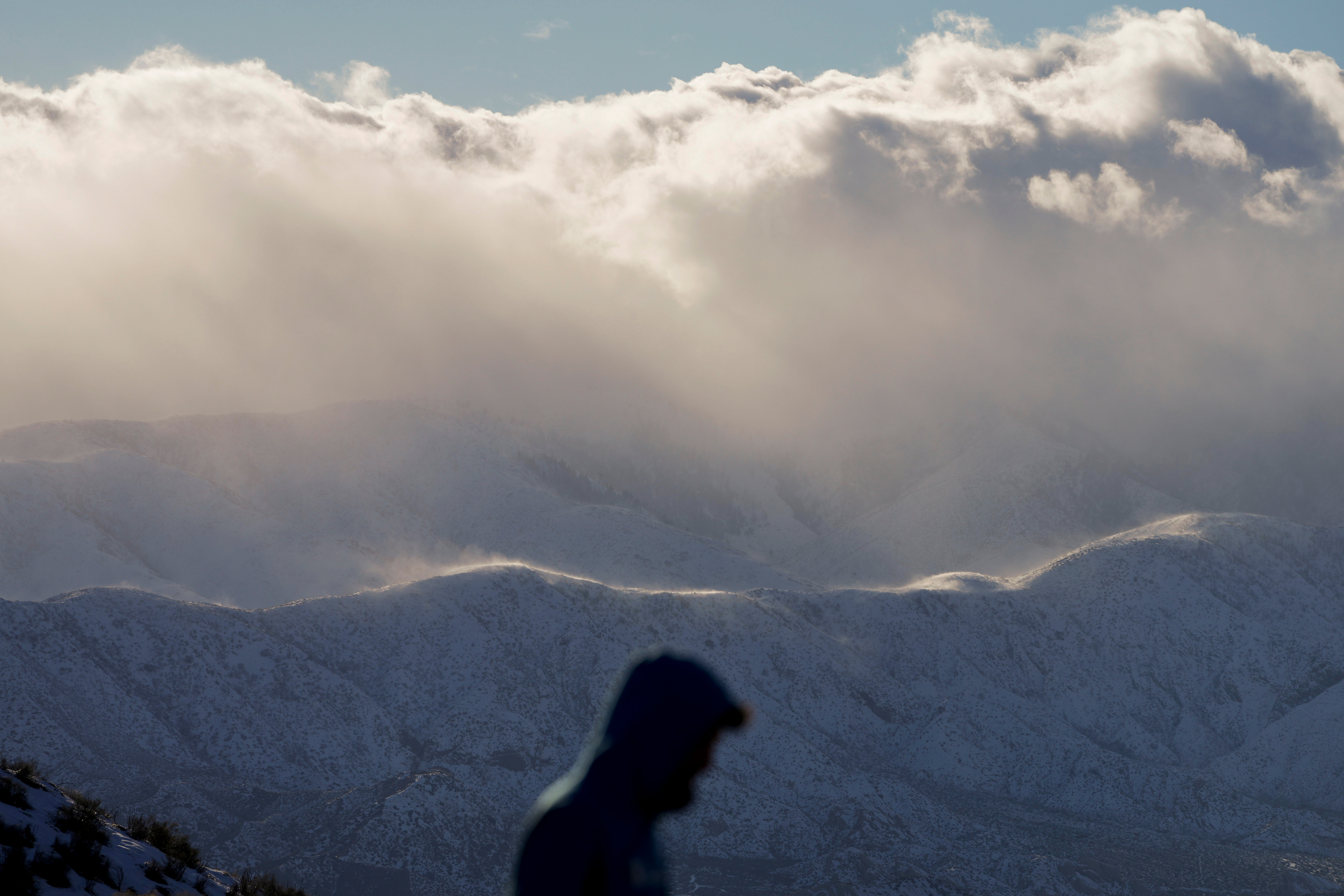 A visitor at a scenic outlook is backdropped by snow-covered mountains near Hesperia, California on Wednesday, March 1, 2023. (Photo: Jae C. Hong, AP)
