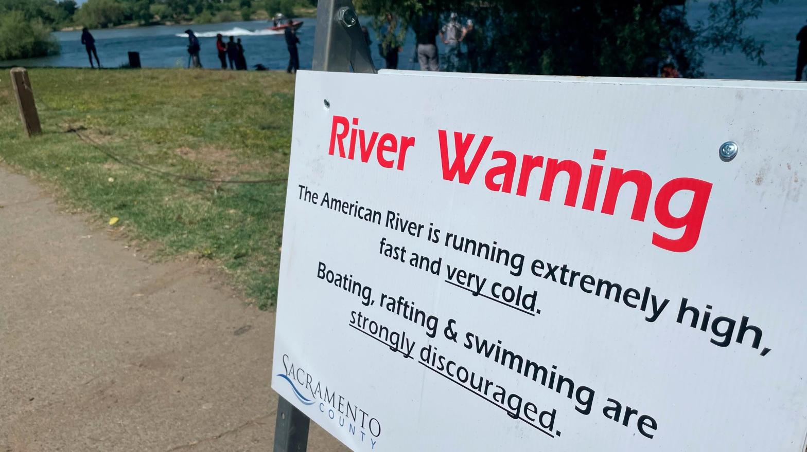 A sign warning the public of dangerous river conditions is posted alongside the American River in Sacramento, California on May 23, 2023.  (Photo: Haven Daley, AP)